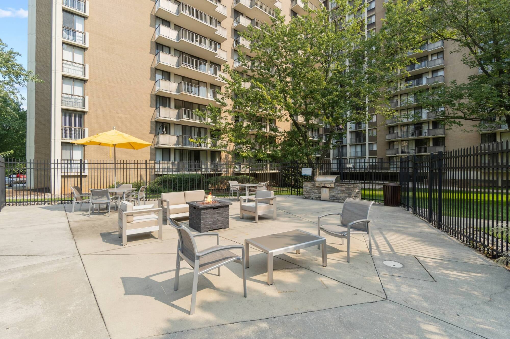 Milestone Apartments Outdoor patio with Adirondack chairs around a fire pit, surrounded by trees and apartment buildings.
