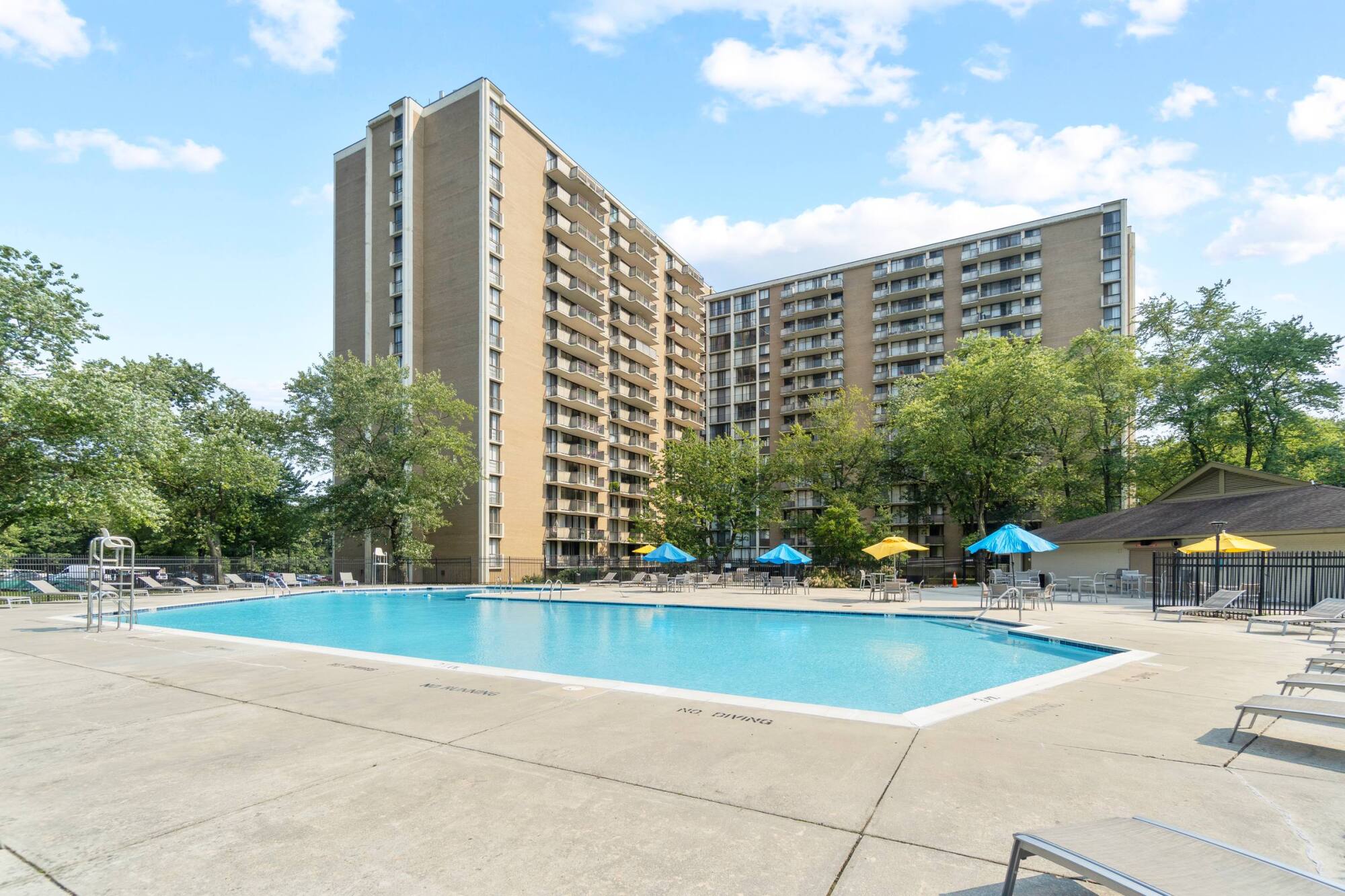 Milestone Apartments Outdoor patio with Adirondack chairs around a fire pit, surrounded by trees and apartment buildings.