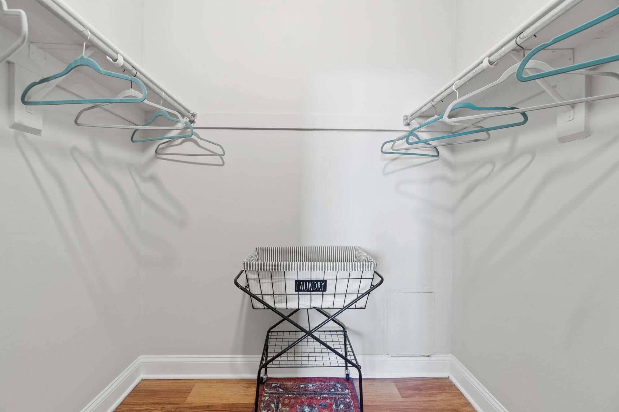 Empty walk-in closet with white walls, several teal hangers, a laundry basket, and a small rug on a wooden floor.