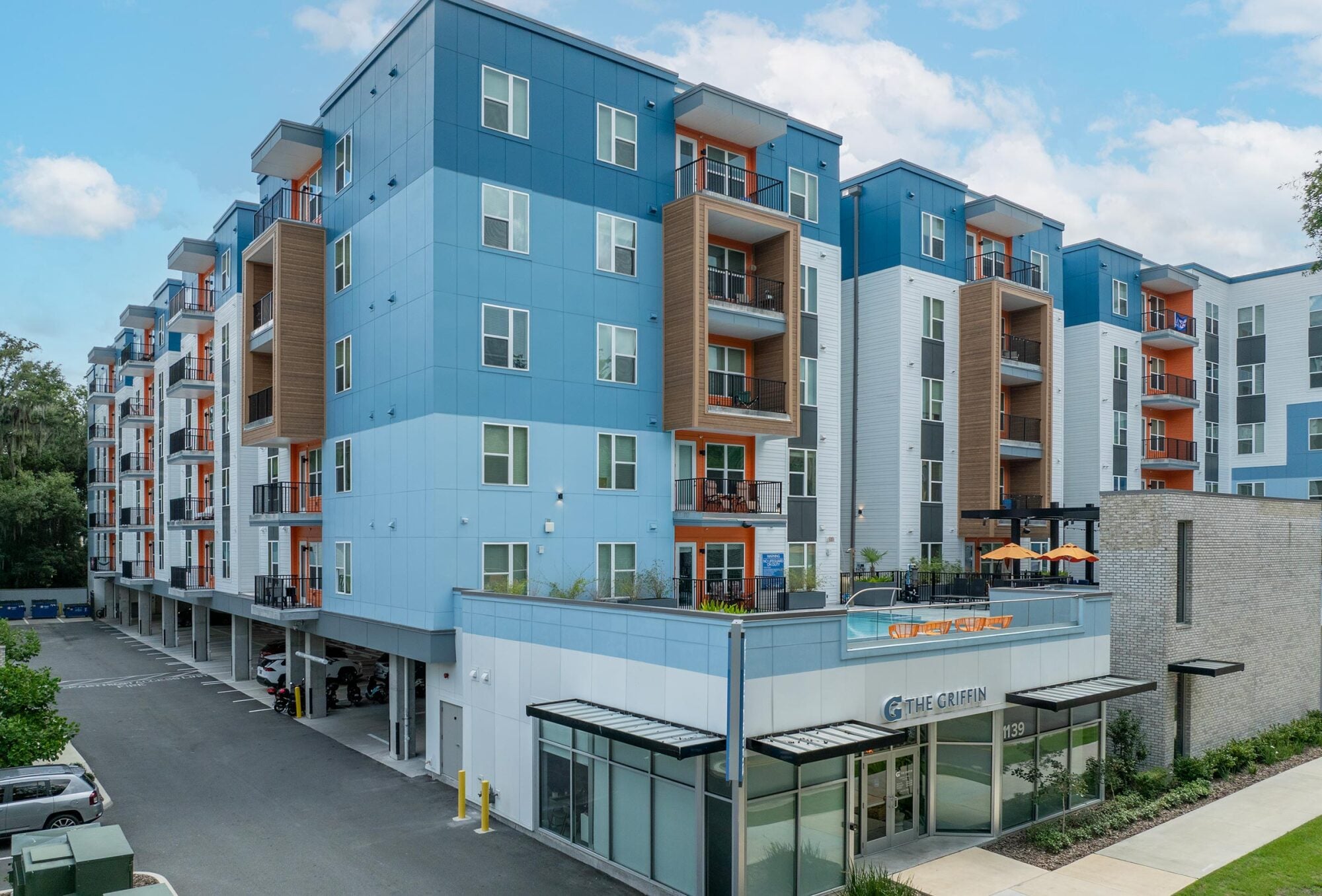 Modern blue and white apartment building with balconies and ground-floor glass entrance on a sunny day.