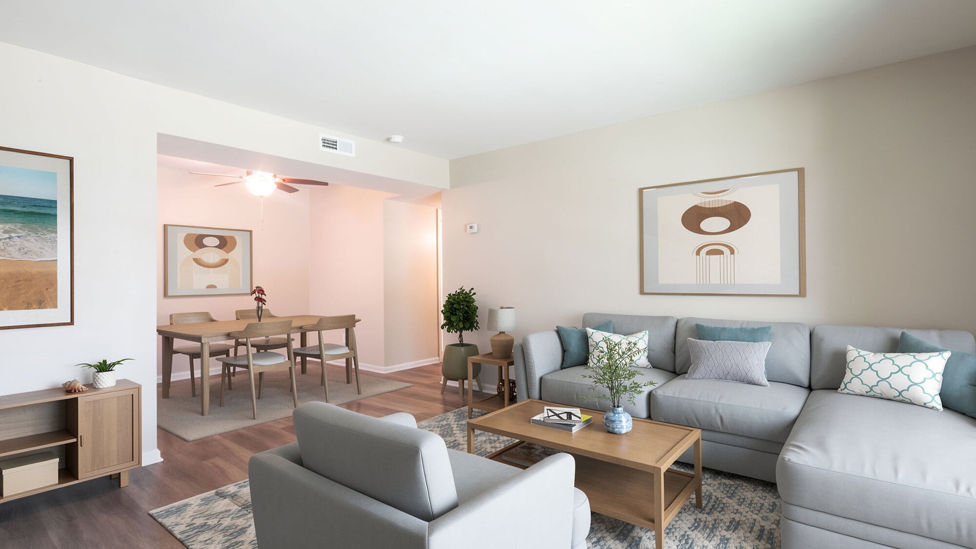 Modern living room with gray furniture, wooden coffee table, abstract art, and dining area with table and chairs in the background.