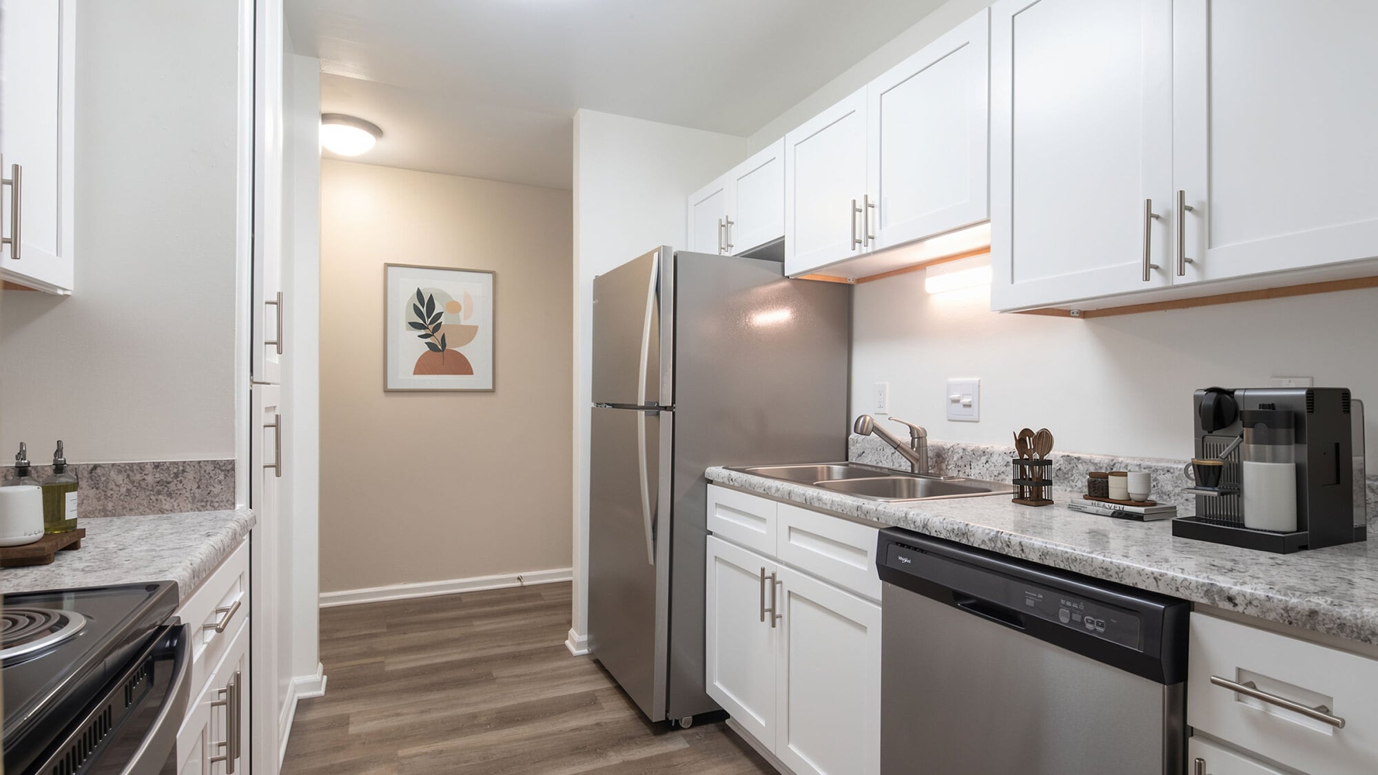 Modern kitchen with white cabinets, stainless steel appliances, granite countertops, and a framed art piece on the back wall.