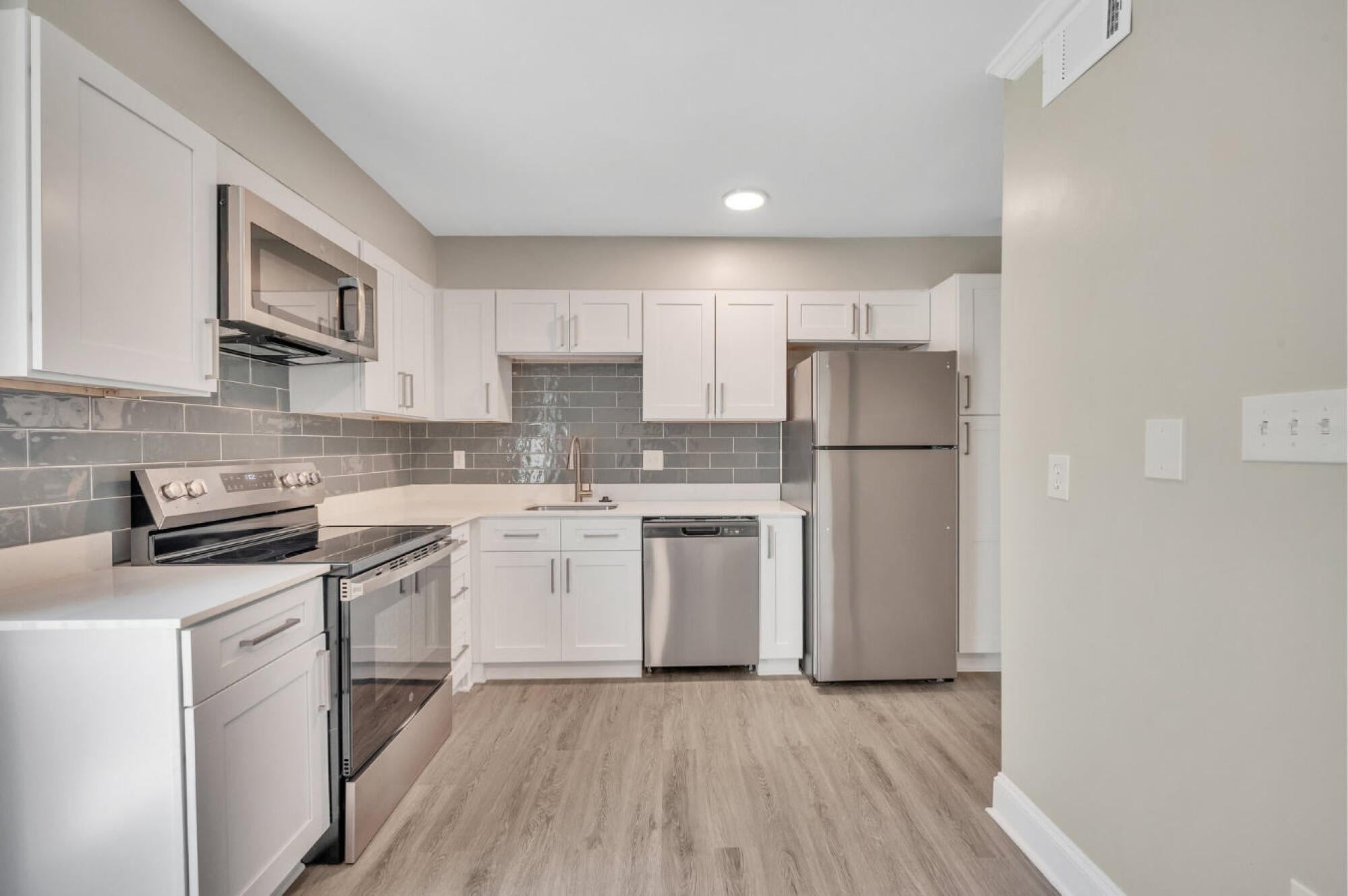Renovated kitchen at Townes at University in Charlotte, NC, with white shaker cabinets, stainless steel appliances and a tile backsplash.