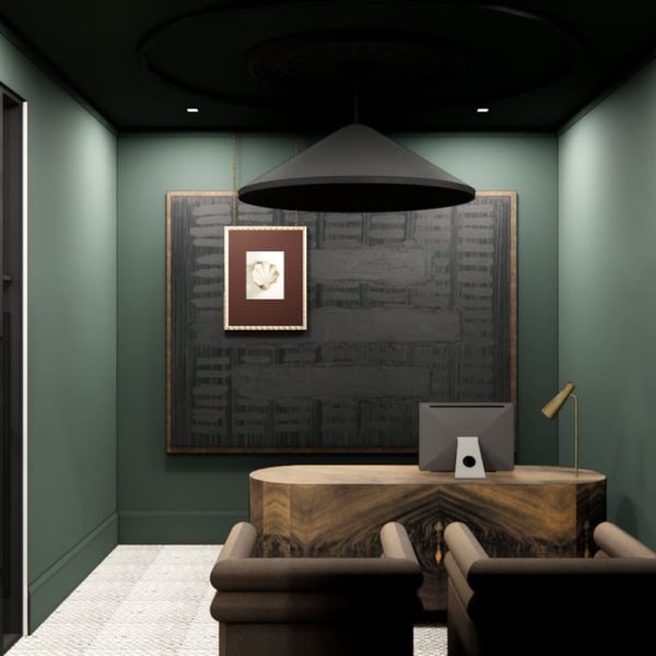 A dark green wall with a framed picture and a table with a lamp on it.