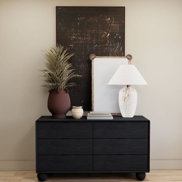 A black dresser with a mirror, lamp, and plant on top.