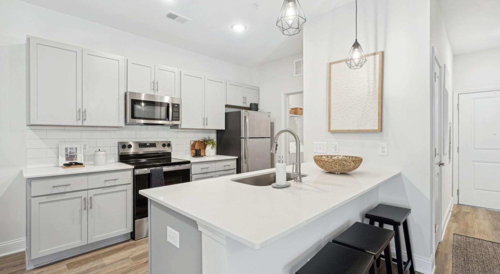 Modern kitchen with white cabinets, stainless steel appliances, pendant lights, and a white island with three black stools.
