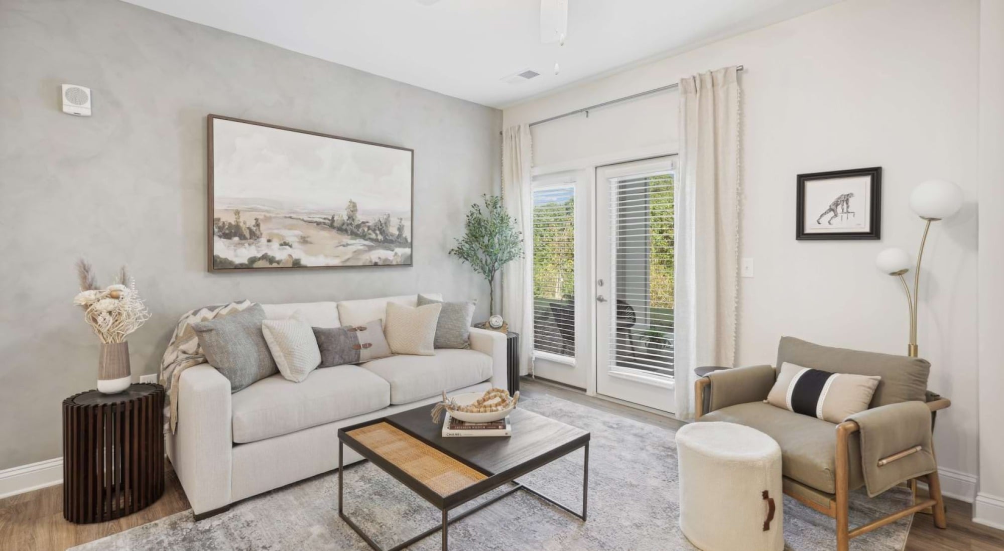 Modern living room with a sofa, armchair, coffee table, art on the wall, and glass doors letting in natural light.