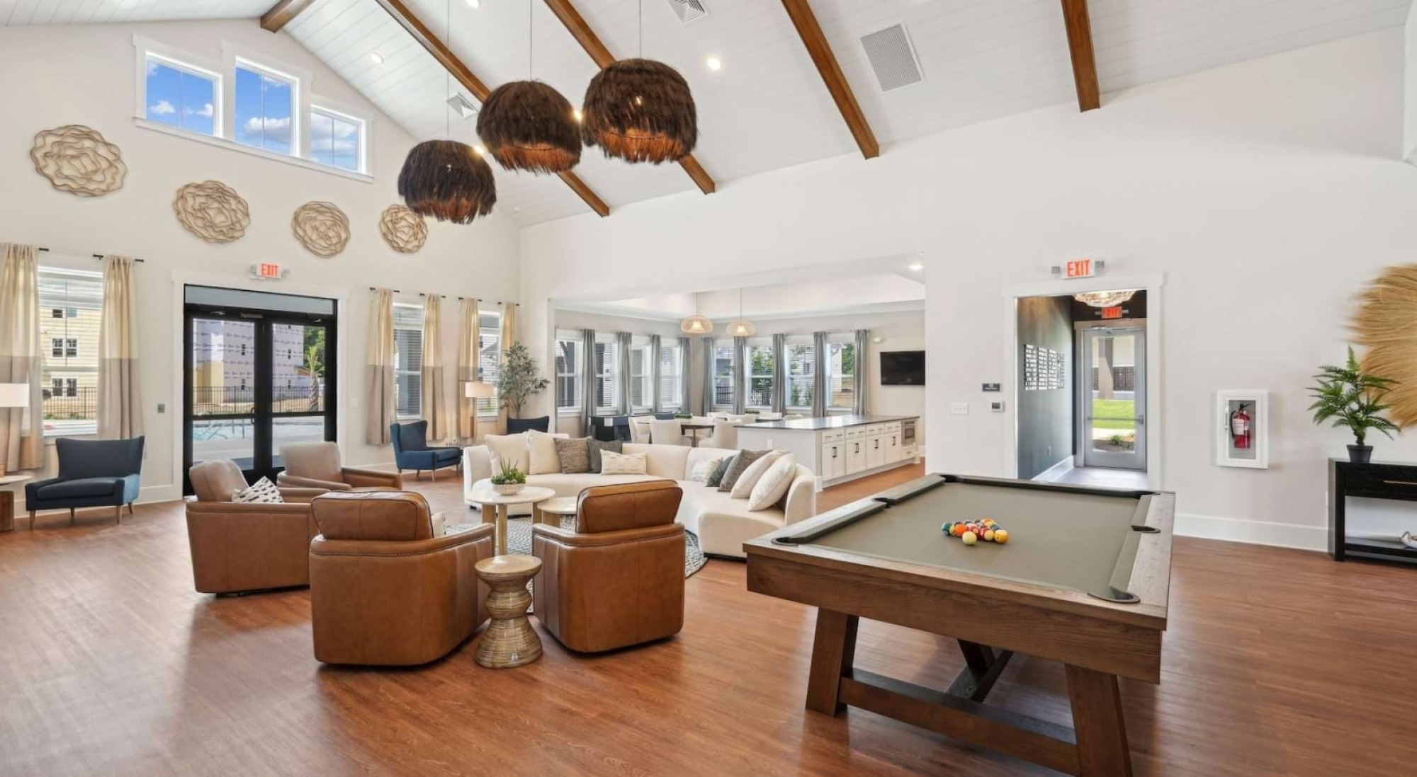 Spacious lounge with pool table, seating area, large windows, and hanging lights, featuring modern decor and wooden floors.