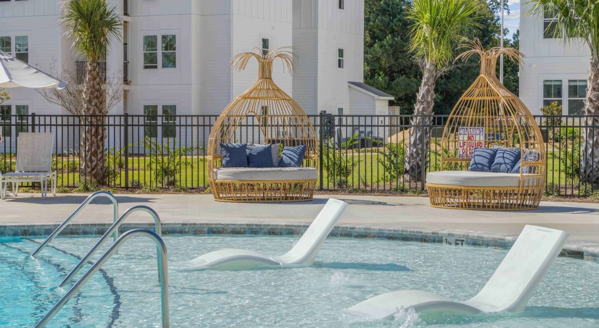 Two wicker lounge chairs and two white pool loungers sit beside a bright, inviting outdoor swimming pool.