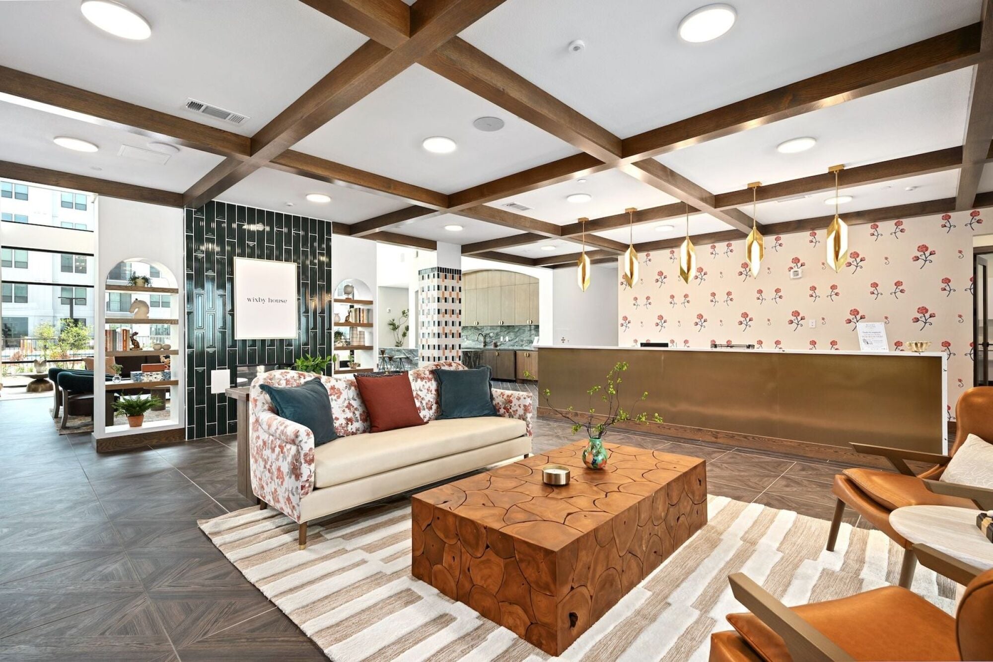 Wixby House lobby in Austin, TX featuring a patterned sofa, wood coffee table, leather lounge chairs, brass pendant lighting, floral wallpaper, and a modern reception desk.