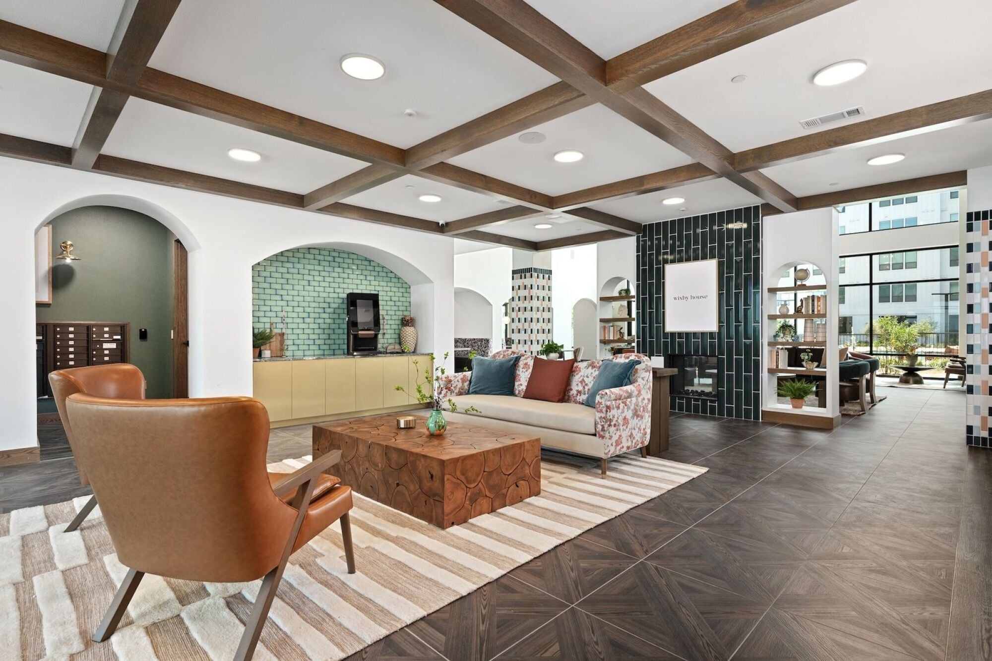 Wixby House lobby in Austin, TX featuring a patterned sofa, wood coffee table, leather lounge chairs, brass pendant lighting, floral wallpaper, and a modern reception desk.