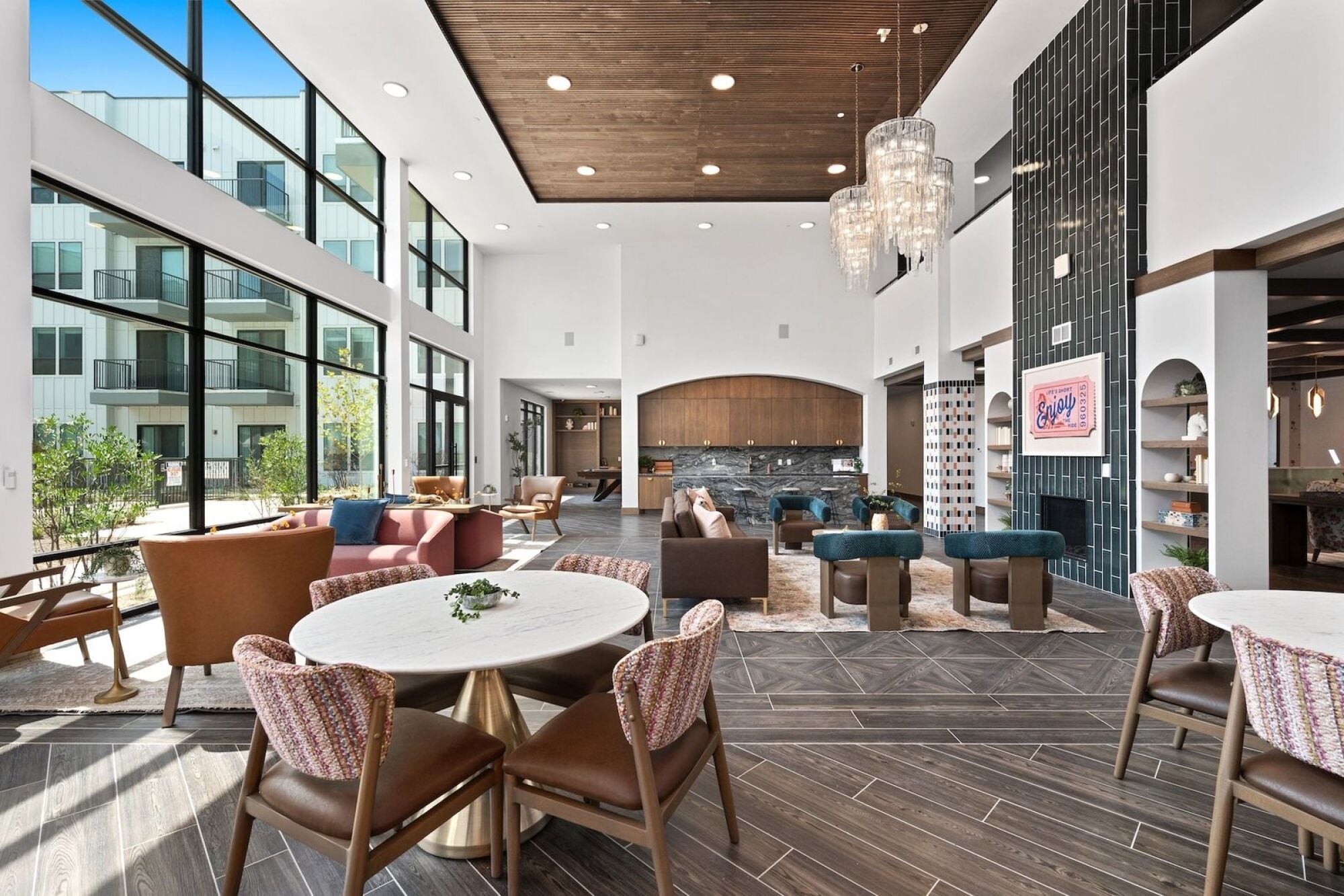 Wixby House clubroom in Austin, TX featuring comfortable lounge seating, dining tables, colorful accent chairs, floor-to-ceiling windows, and a modern fireplace.