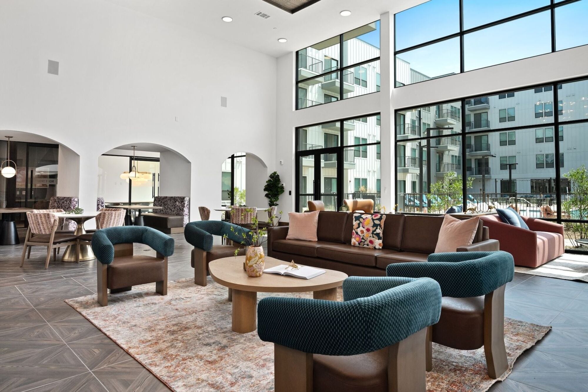 Wixby House clubroom in Austin, TX featuring comfortable lounge seating, dining tables, colorful accent chairs, floor-to-ceiling windows, and a modern fireplace.