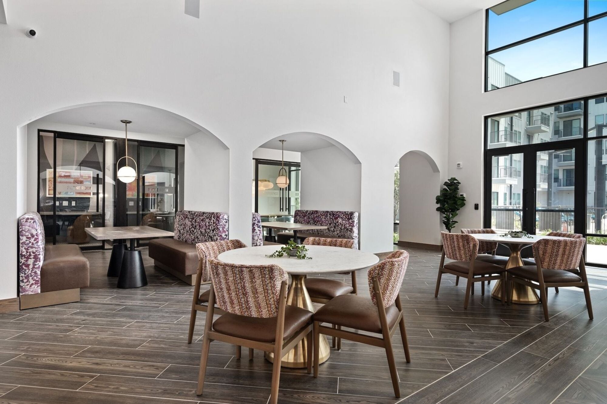 Wixby House clubroom in Austin, TX featuring dining tables, patterned lounge seating, arched architectural details, and floor-to-ceiling windows.