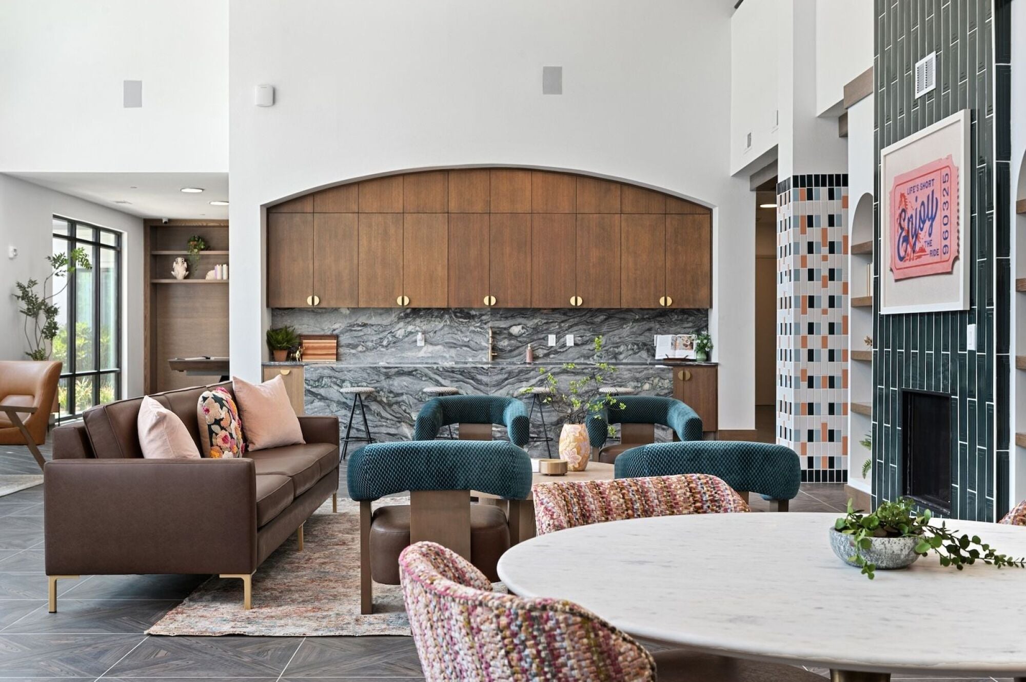 Wixby House clubroom in Austin, TX featuring a cozy lounge area with a sofa, teal accent chairs, a marble-topped kitchen with wood cabinetry, and a decorative fireplace.