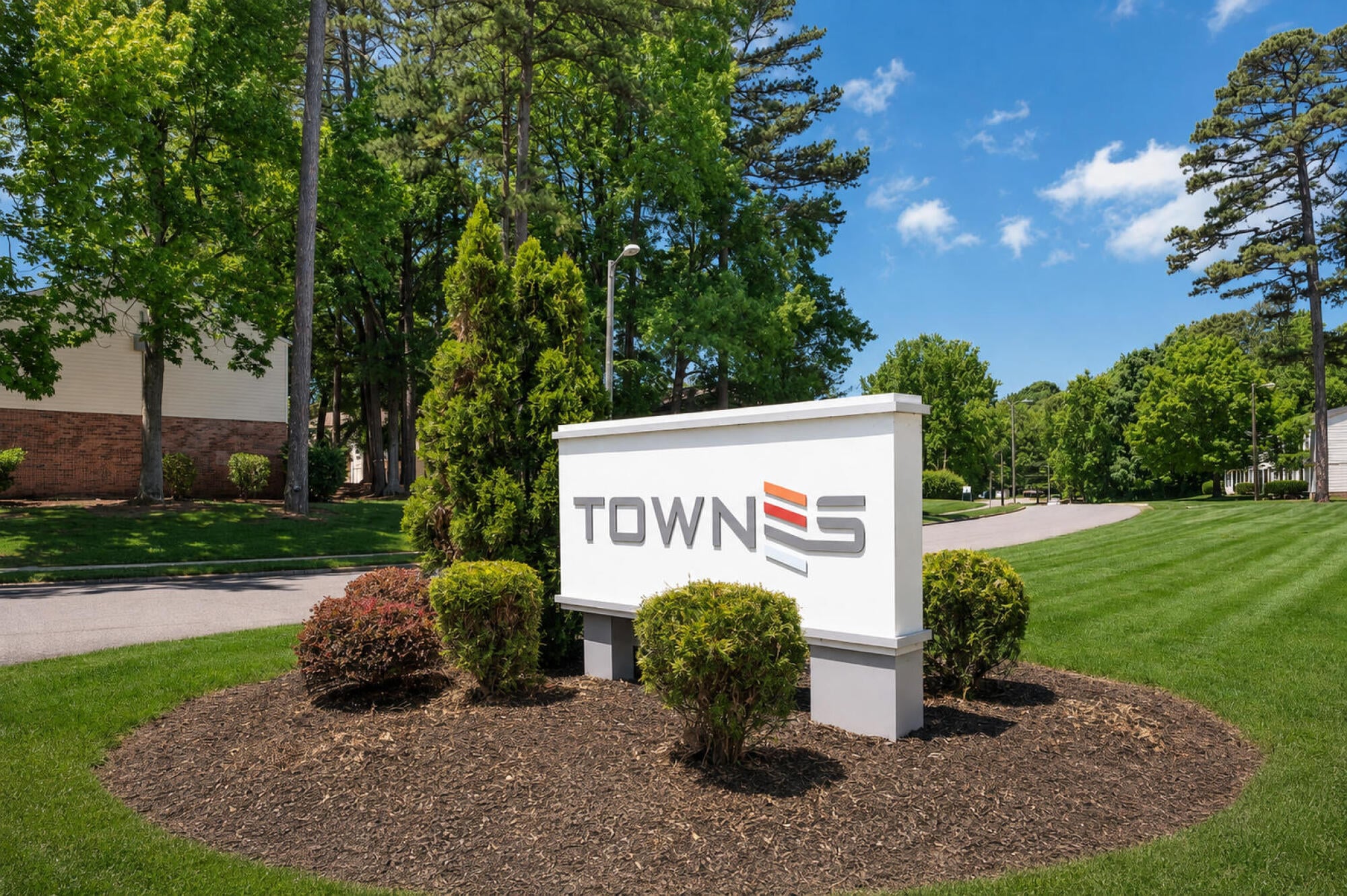 Townes at University monument signage set among evergreens and flowering shrubs at the community entrance in Charlotte, NC.