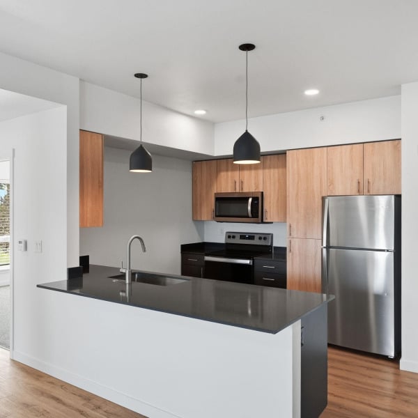 Dark quartz peninsula counter with pendant lighting in a Cypress apartment kitchen in Redmond, Oregon.