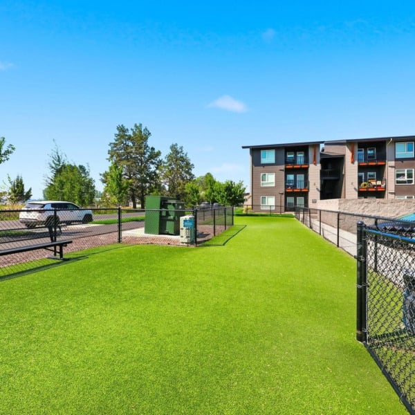 Fenced off-leash dog run with turf and shaded bench seating at Cypress apartments in Redmond, Oregon.