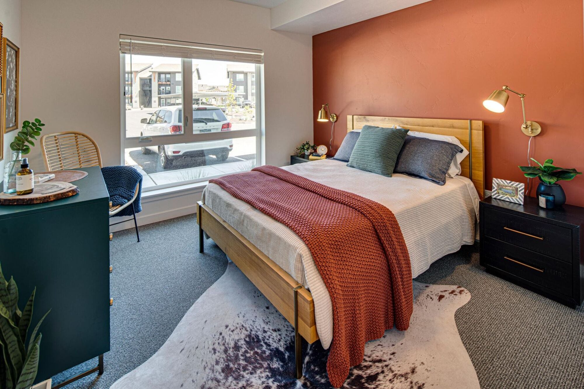 Furnished model bedroom with a warm terracotta accent wall at Cypress apartments in Redmond, Oregon.
