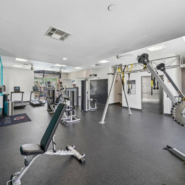 Strength training machines and a weight bench in the fitness center at Ontario Town Square Townhomes in Ontario, CA.
