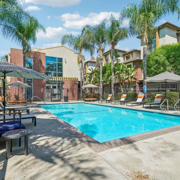 Pool deck at Ontario Town Square Townhomes in Ontario, California, lined with lounge chairs, umbrellas, and shade cabanas.