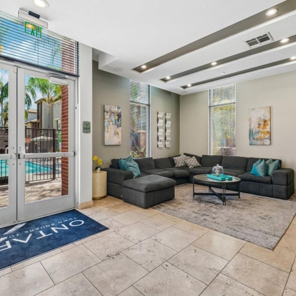 Resident lounge at Ontario Town Square Townhomes in Ontario, California, with sectional seating and glass doors opening to the pool deck.