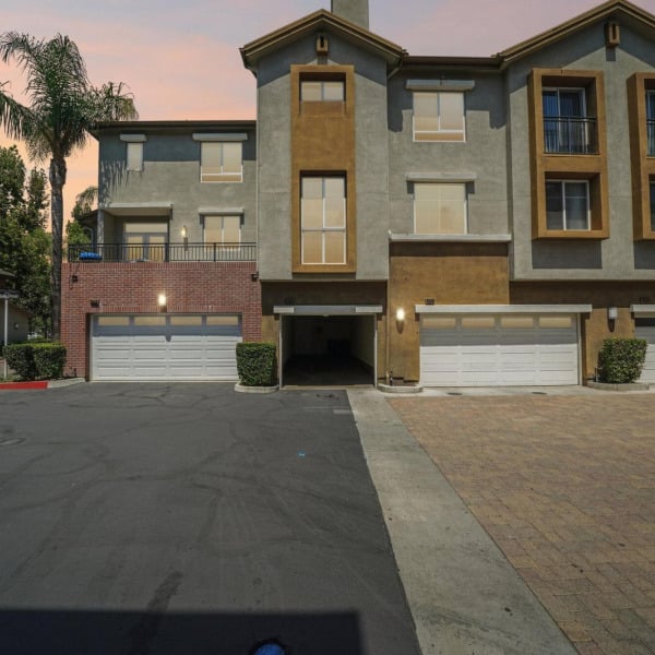 Townhome exteriors at dusk at Ontario Town Square Townhomes in Ontario, California, with attached two-car garages along the drive.
