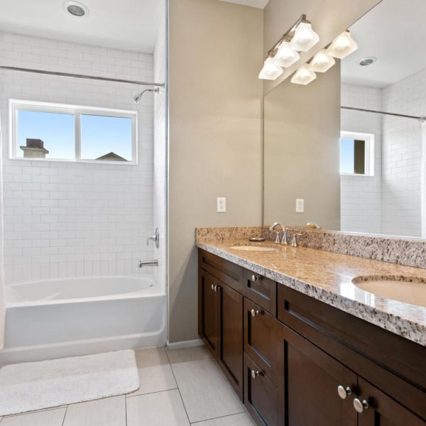 Townhome bathroom with double vanity, granite counter, and a tub-shower at Ontario Town Square Townhomes in Ontario, California.