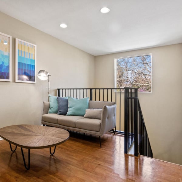 Living room in a townhome at Ontario Town Square Townhomes in Ontario, California, with hardwood-style floors and an open stair rail.