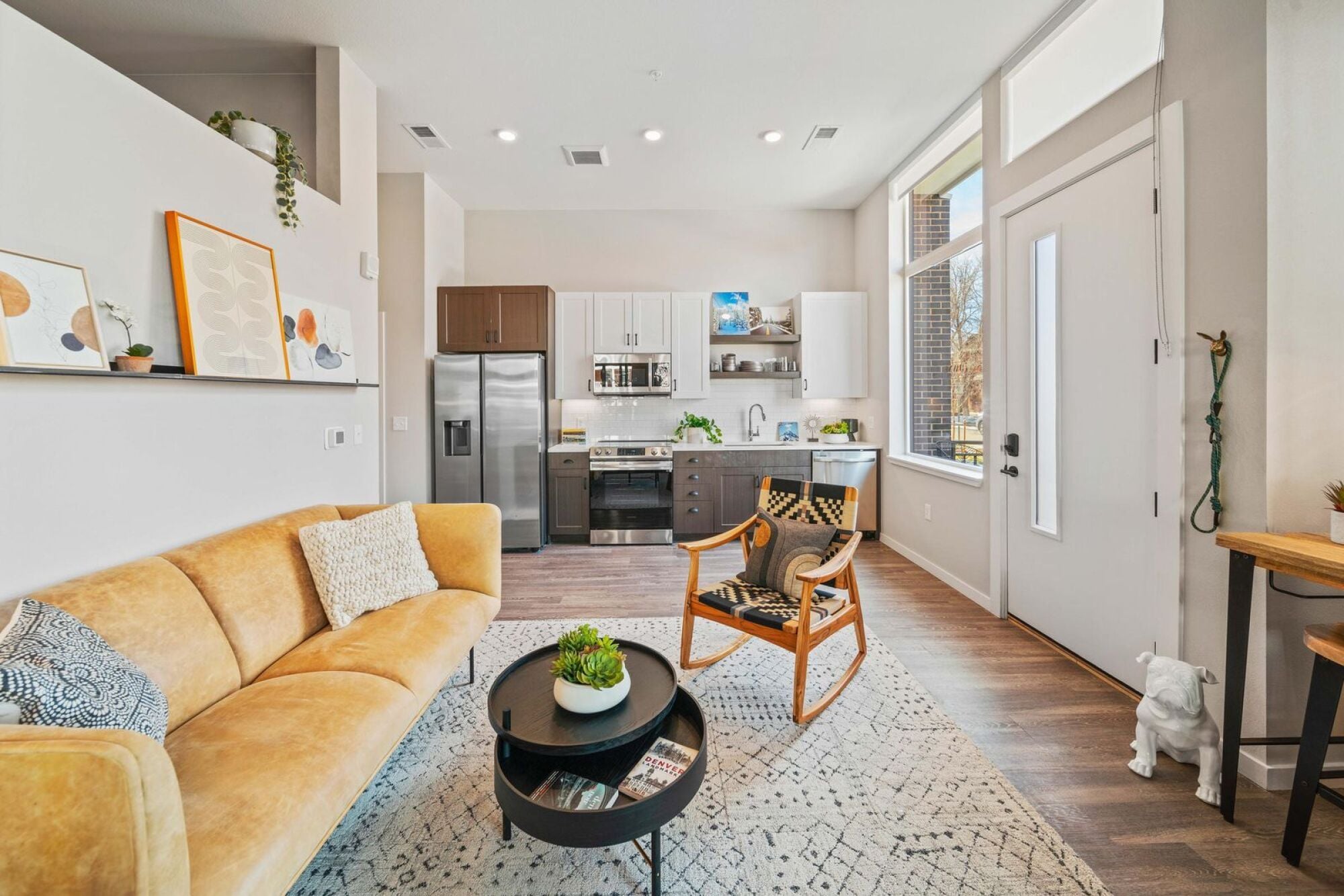 A woven mid-century armchair with patterned throw pillows adds character to this Jayne apartment living space in Denver, CO.