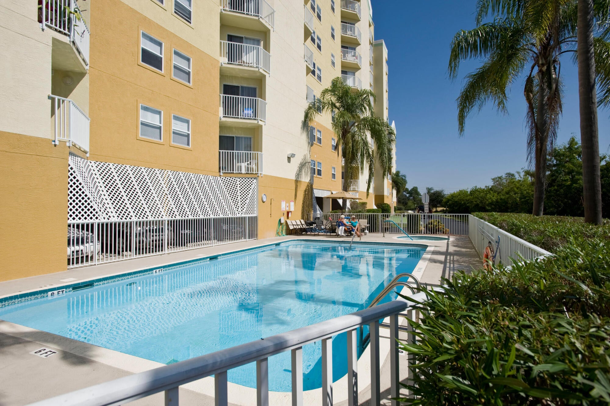 Residents relaxing poolside among palm trees at The Landings at Sea Forest 55+ apartments in New Port Richey, FL.