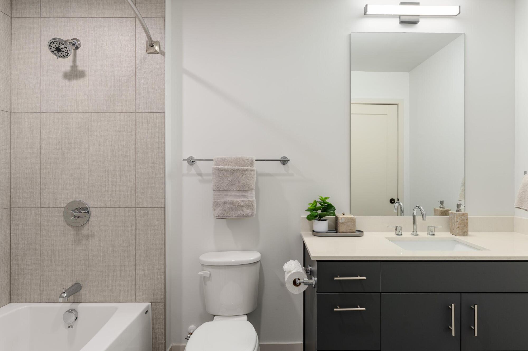 Bathroom with a tiled tub and shower combination, dark vanity, light countertop and mirror