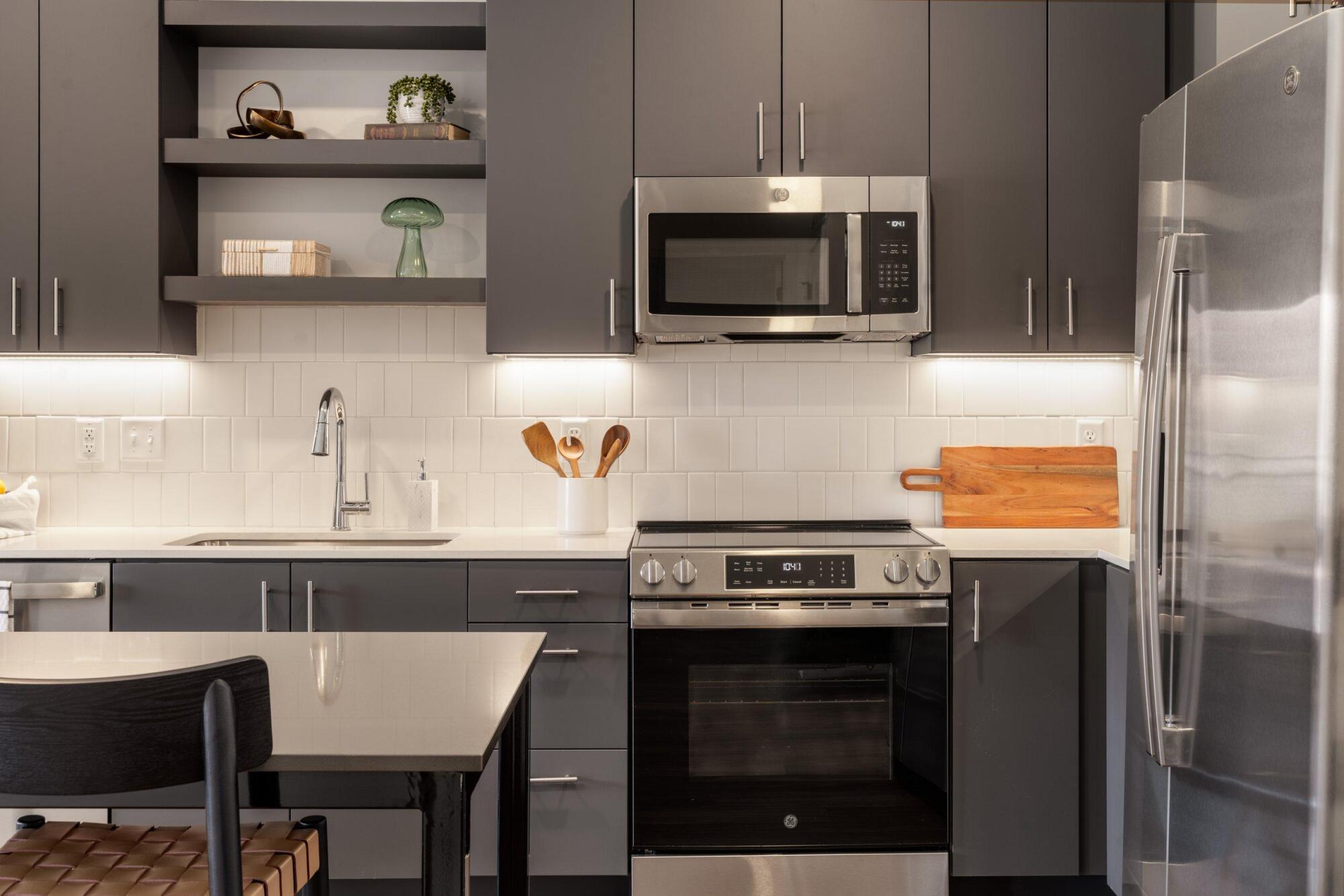 Kitchen with dark cabinets, open shelves, white tile backsplash, stainless steel range, microwave and refrigerator