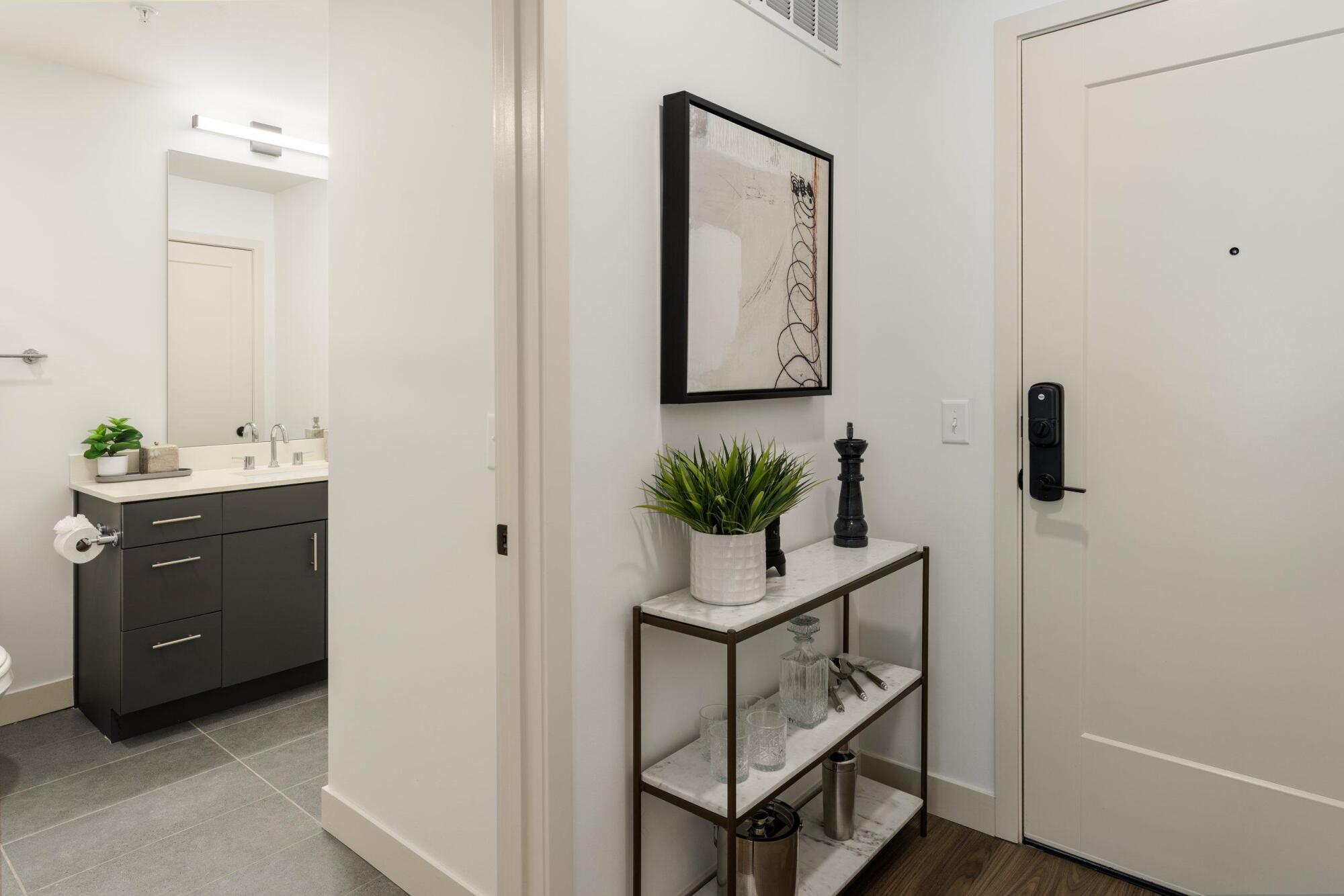 Apartment entry with a keypad smart lock, a console shelf with plants and a view into the bathroom