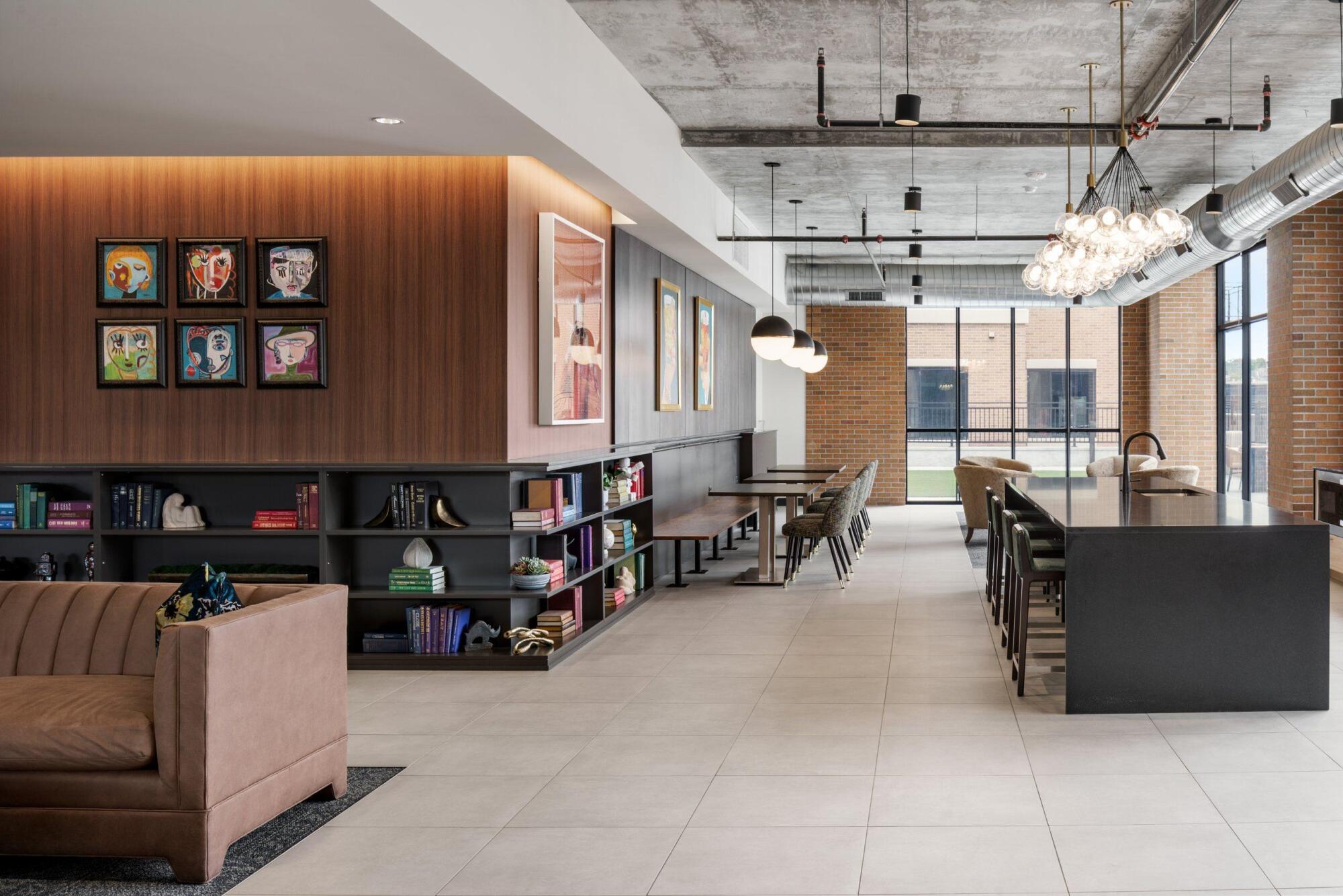 Clubroom lounge with a velvet sofa, library shelving, framed art and a long kitchen island with bar seating