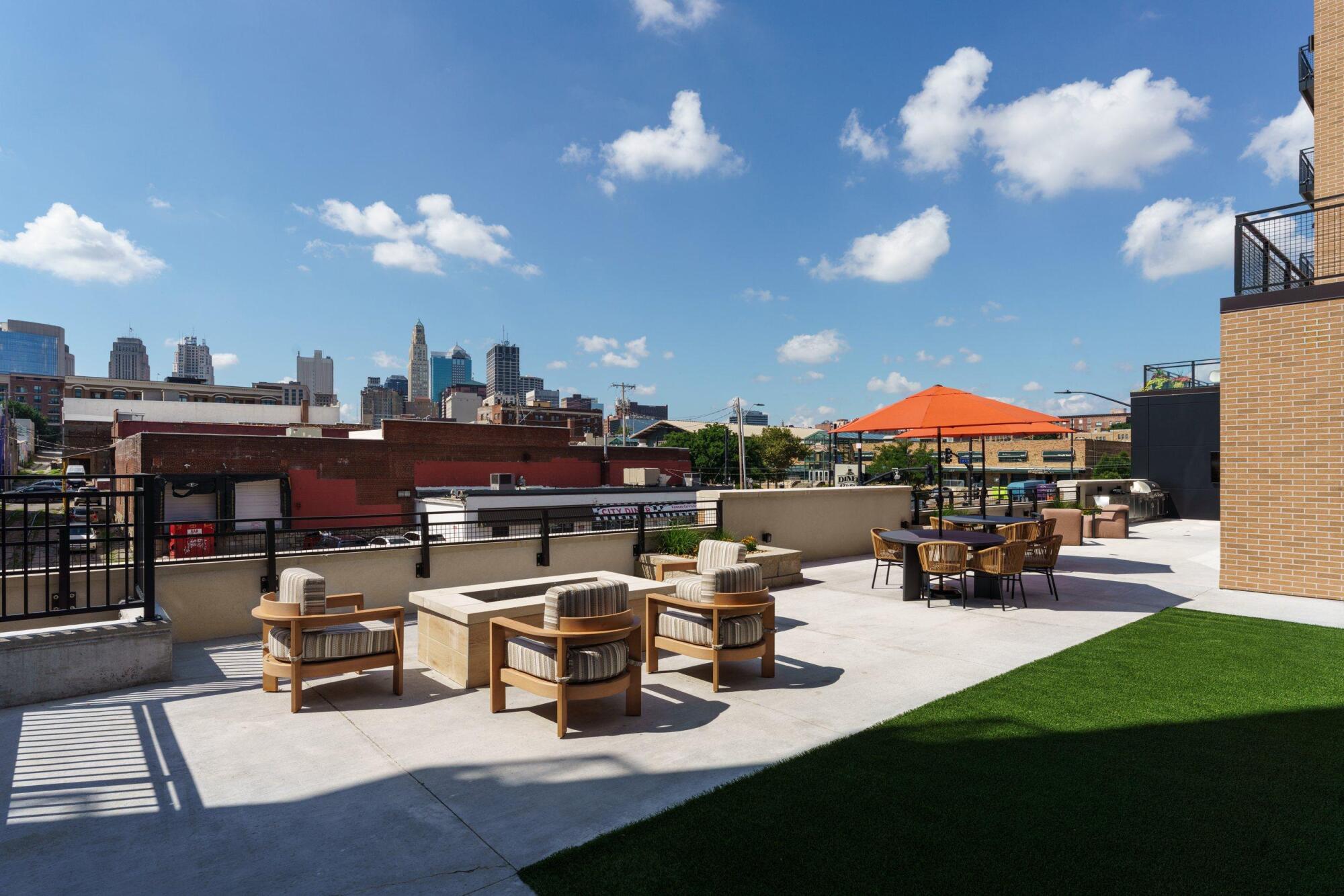 Outdoor terrace with fire pit seating, dining tables and orange umbrellas overlooking the downtown Kansas City skyline