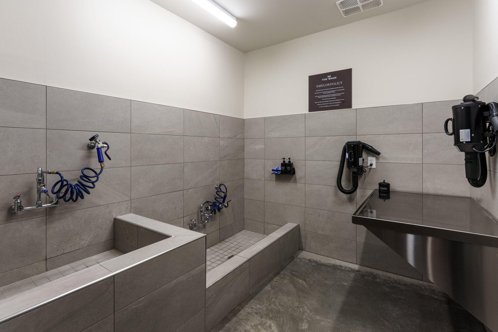 Pet washing station with two tiled tubs, handheld sprayers, a stainless grooming table and wall-mounted pet dryers