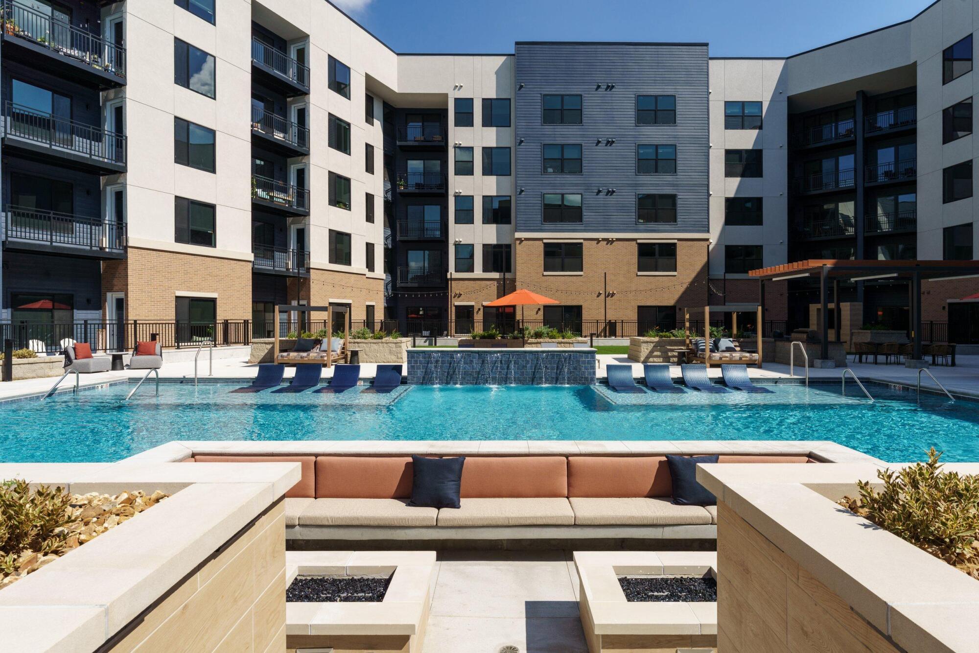 Sunken lounge with cushioned built-in seating and fire tables facing the pool, loungers and a water wall