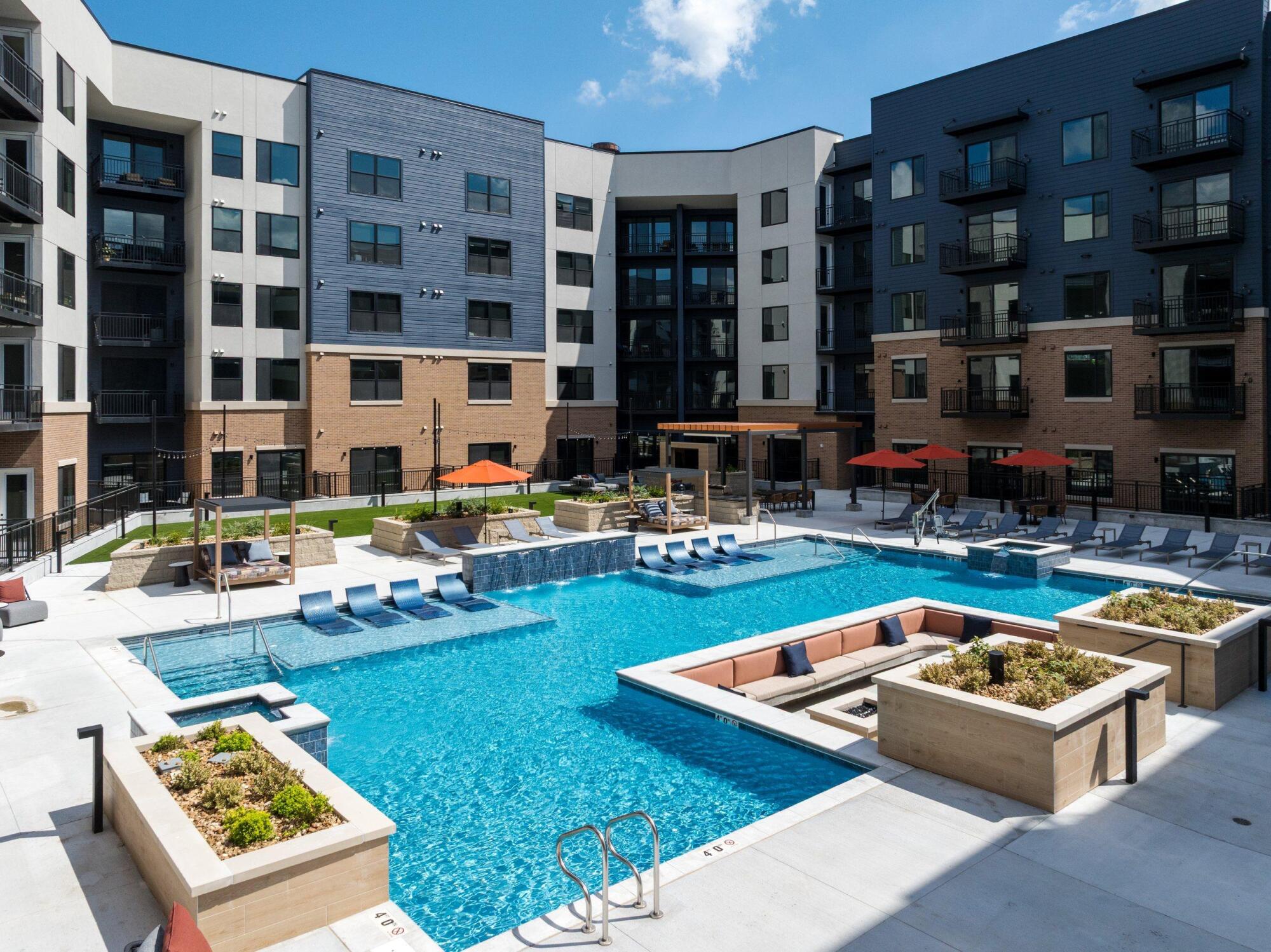 Aerial view of the pool with in-water loungers, a sunken fire lounge, planters and umbrellas, surrounded by the building