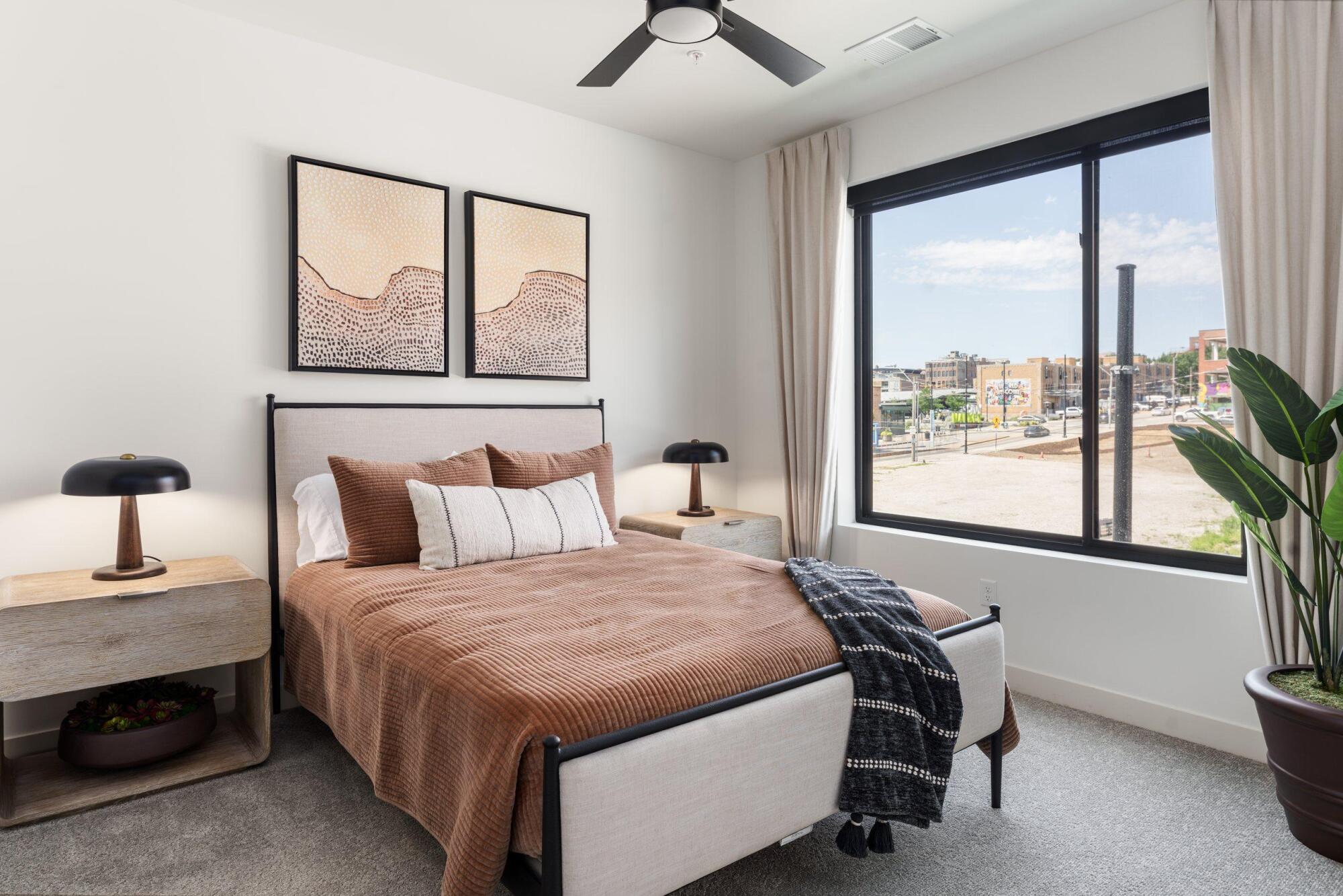 Bedroom with an upholstered bed, two nightstands, a ceiling fan and a large window with neighborhood views
