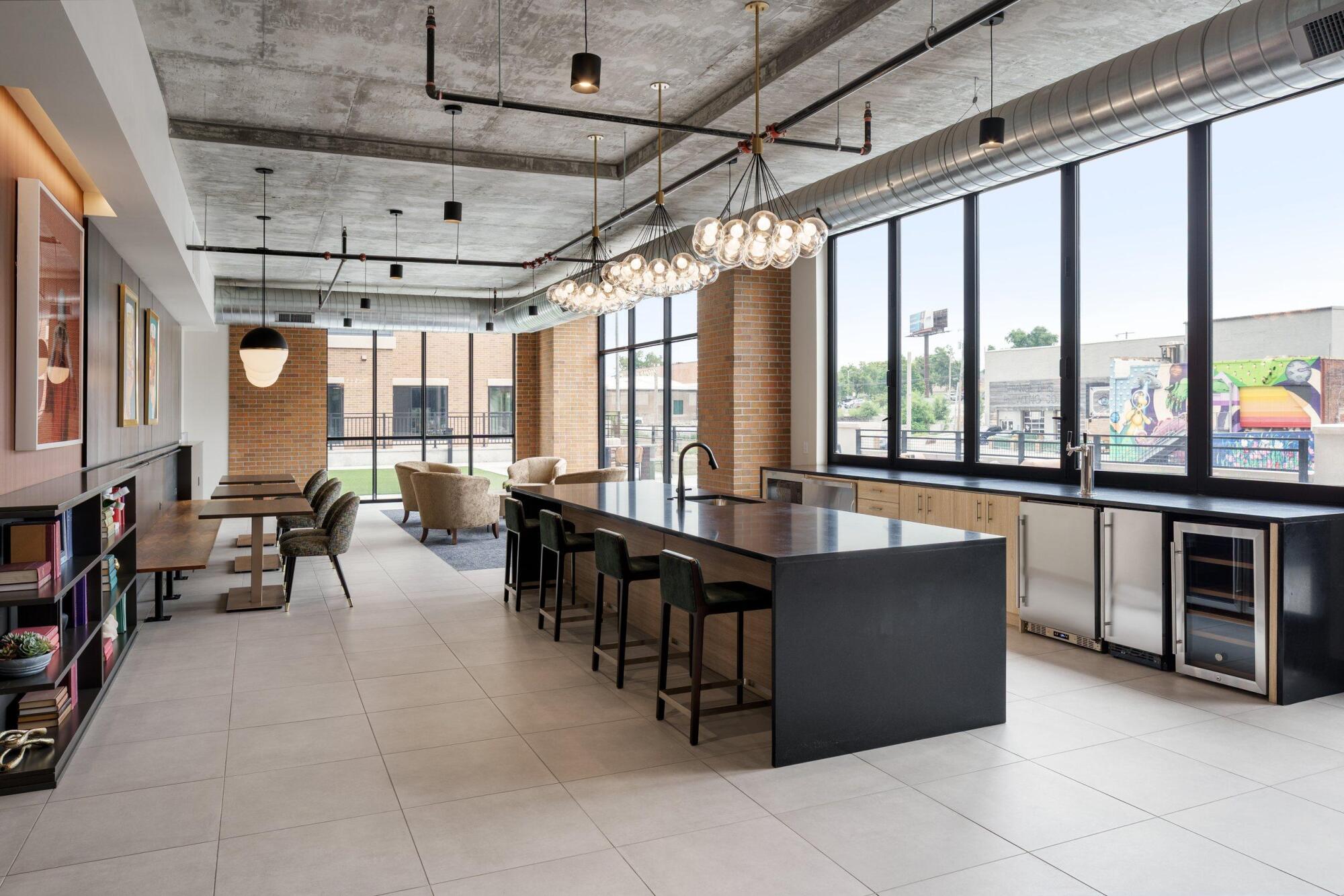 Clubroom with a long black island, bar stools, beverage fridges, globe pendant lights and floor-to-ceiling windows