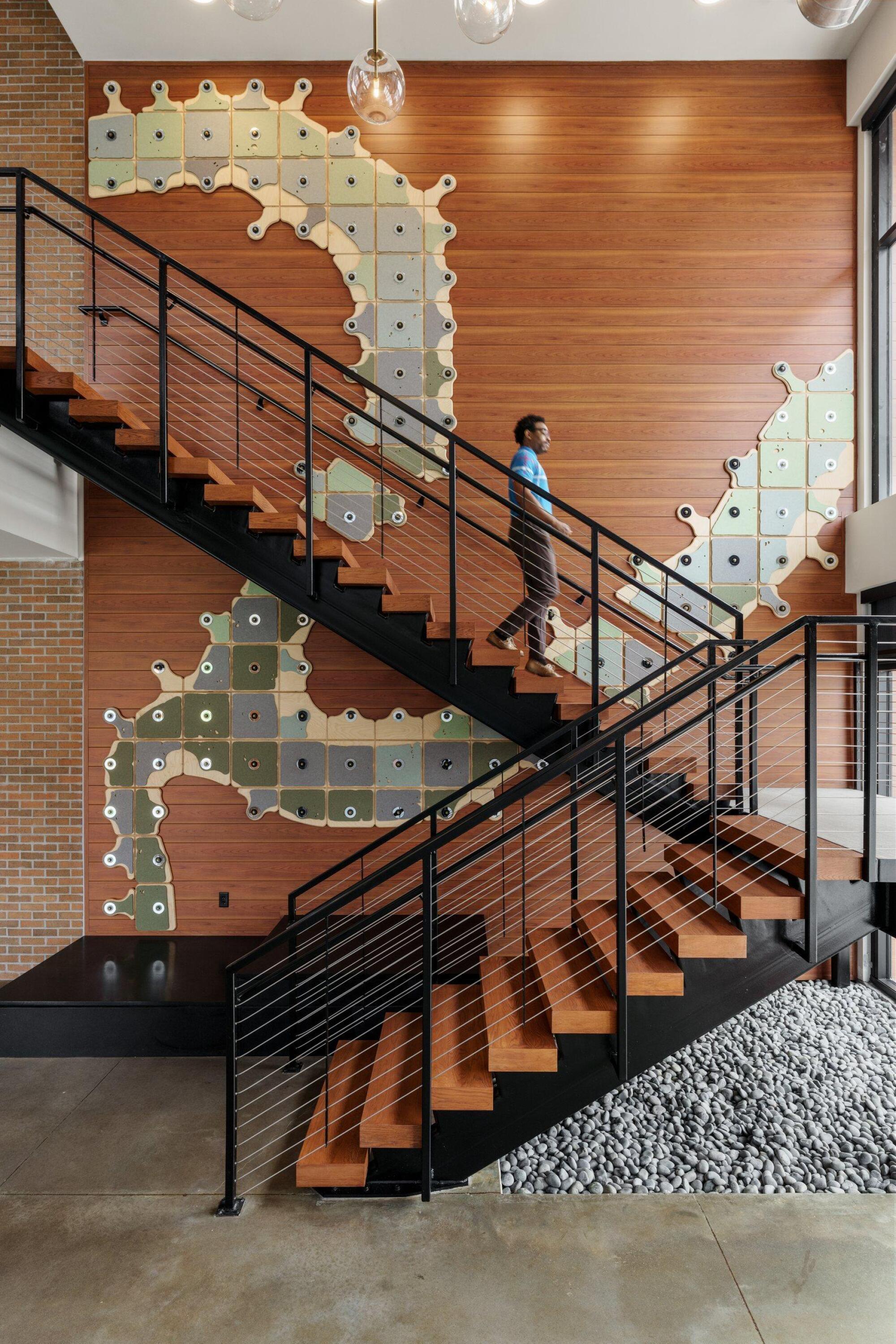 Resident walking up a floating steel staircase beside a two-story mosaic mural wall in the lobby