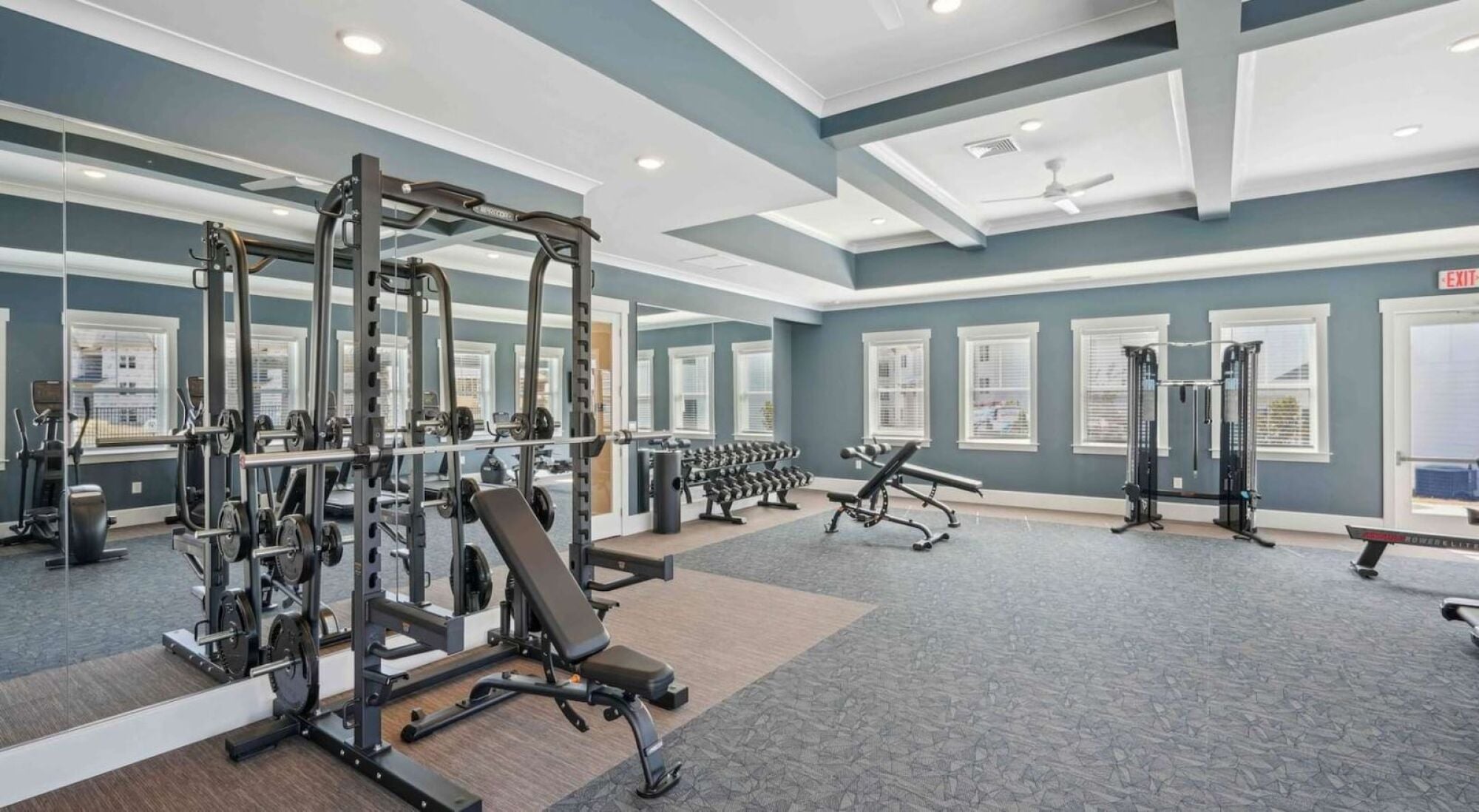 A gym with a variety of equipment including a weight bench, a squat rack, and a treadmill.
