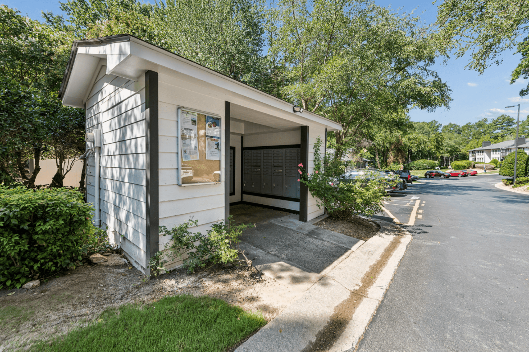 Community mailbox area with covered mail center, landscaped grounds, and parking area at Laurel Springs Apartments