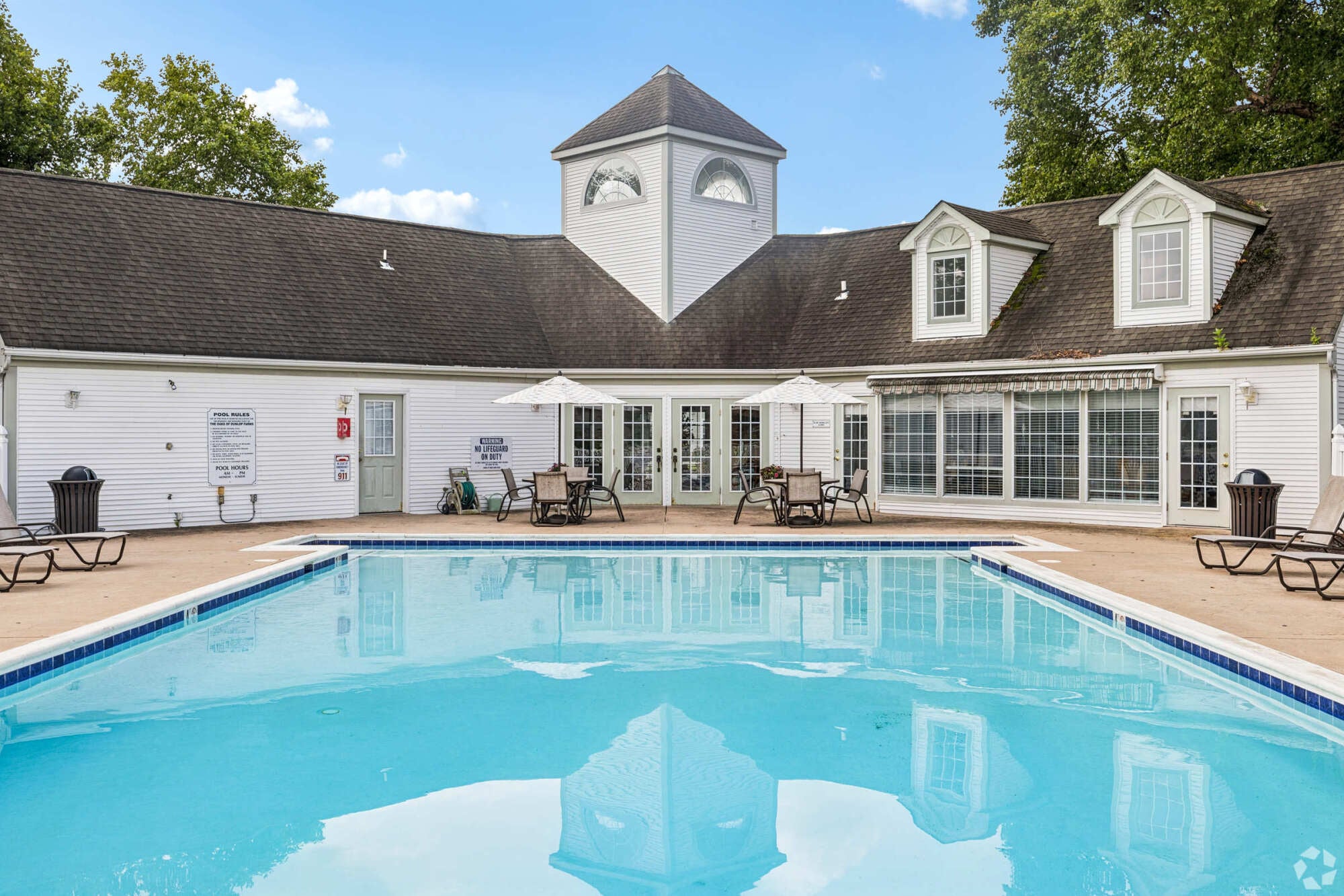Oaks of Dunlop Farms in Colonial Heights, VA, swimming pool with lounge chairs, umbrellas, and the clubhouse beyond.